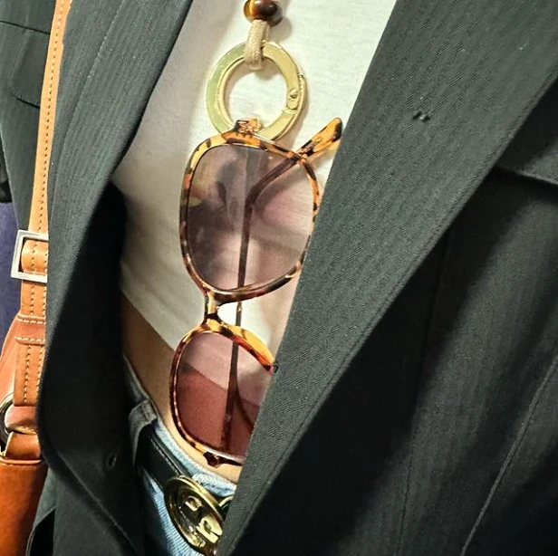 femme qui porte un collier sautoir porte lunette en coton ciré avec un anneau doré. Accroché au sautoir on y retrouve des lunettes.